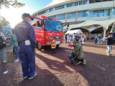 写真:ちびっこ防火衣を着て消防車の前で写真を撮っている様子です。令和5年10月28日