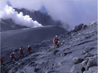 噴火している背景で捜索する救助隊員の写真