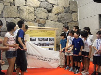 写真:子ども達をはじめとする参加者が左右からひもを引き除幕している瞬間