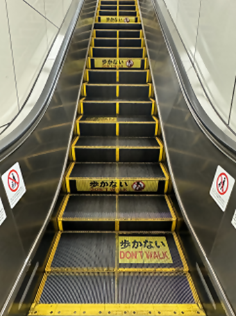 写真：マーキングを施したエスカレーターの画像。表面に「歩かない　DON’T WALK」とマーキングされている。