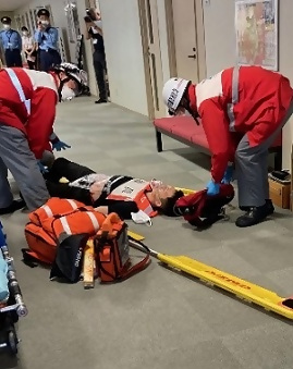 写真：負傷して担架に乗せられる職員役の男性