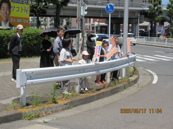 写真：区役所前交差点でサイン版を掲げて交通安全の呼びかけをしている様子です。