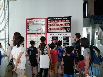 写真：選手の紹介や順位表、試合スケジュールが掲載されているのボードの説明を受けている様子1