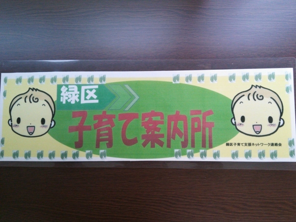 写真：左右に赤ちゃんのイラストがあり、中心に緑色の背景に白い字で「緑区」、赤い字で「子育て案内所」と書かれた、横長の看板です。
