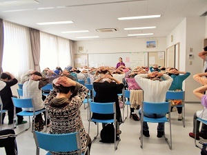 写真：野並コミュニティセンターで椅子に腰かけて運動する参加者たち