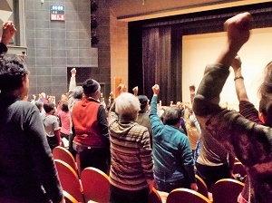 写真：会場内で座席から立って運動をしている参加者たち