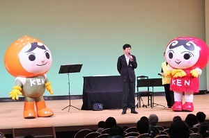 写真：ステージ上で、人権イメージキャラクターたちの間に立って挨拶をする区長