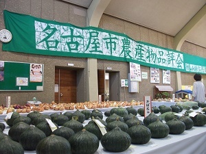 写真：名古屋市農産物品評会の垂れ幕と、その下に並ぶ野菜の様子