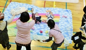 写真：ねんねdeフォトのコーナーで子どもを大きな絵の上に寝かせて撮影する様子