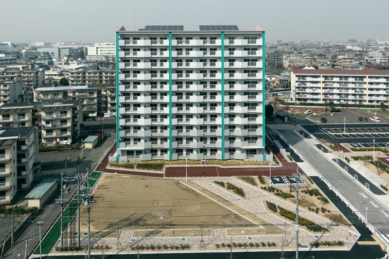 写真：南面バルコニー側の正面の鳥瞰的外観。屋上太陽光発電パネルが見える。