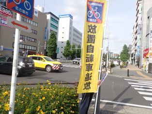 写真：放置自転車追放キャンペーンにて旗をもちながら活動するとともに名東土木事務所が広報車で啓発をしている様子