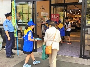 写真:商業施設の入り口で来店者に啓発品を配る防犯少年団の子どもたち