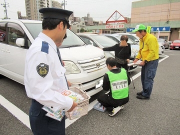 写真:商業施設の駐車場で車にナンバープレート盗難防止ネジを取り付ける様子