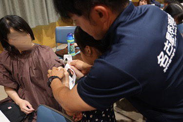 消防職員に教えてもらいながら参加者が三角巾で応急手当をする写真