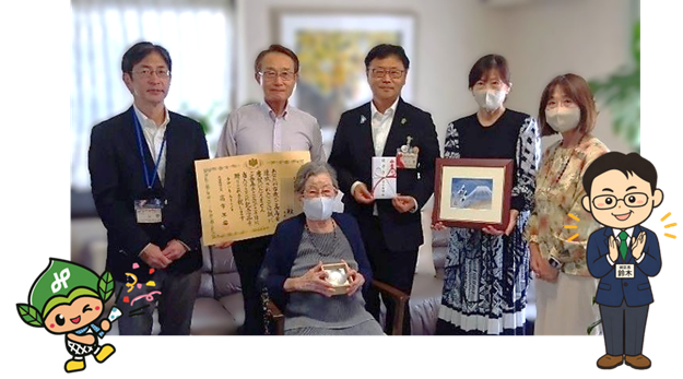 小西さまご家族と区長はじめ区役所職員の写真とみどりっち・区長のイラスト