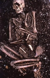 　発掘された2号人骨の写真です。仰向けで、膝を曲げ、腕は胸の前でクロスした体勢をしています。人骨は、まだ遺跡の土の上に載っている状態で、周囲には貝殻や土器片が散らばっています。