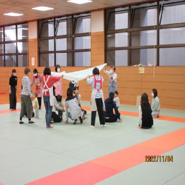 子育てひろばで、大きな布の下で子どもたちが喜んでいる写真です。